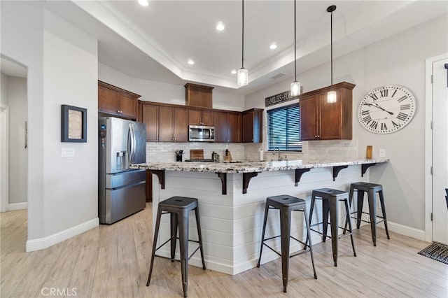 kitchen featuring appliances with stainless steel finishes, hanging light fixtures, light stone countertops, a peninsula, and a tray ceiling