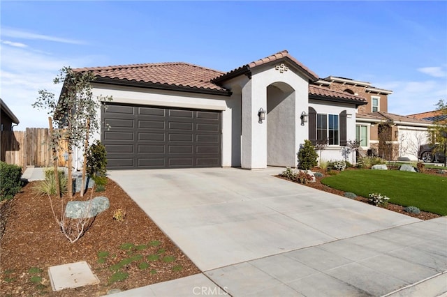 mediterranean / spanish-style house with an attached garage, fence, a tile roof, concrete driveway, and stucco siding