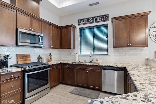 kitchen with light stone countertops, stainless steel appliances, a sink, visible vents, and decorative backsplash