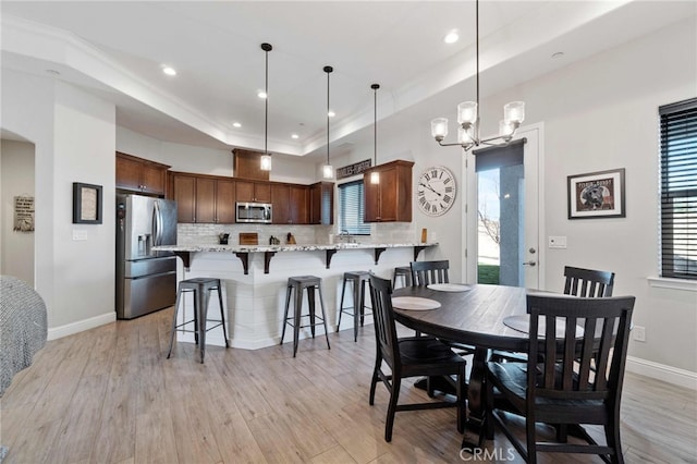 dining area featuring light wood-style flooring, arched walkways, a raised ceiling, and baseboards