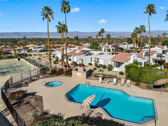 community pool with a patio, a mountain view, fence, a residential view, and a hot tub