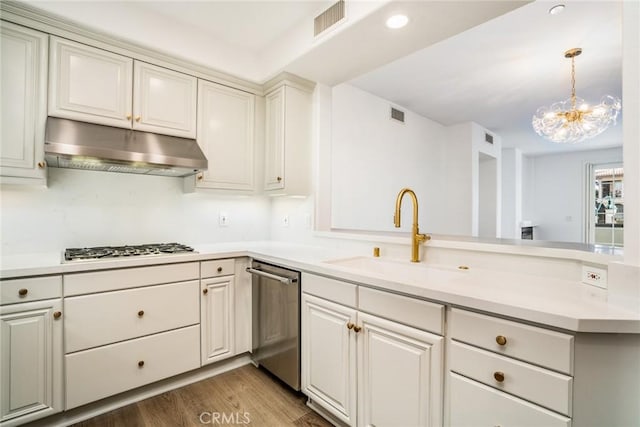 kitchen featuring light countertops, stainless steel dishwasher, a sink, a peninsula, and under cabinet range hood