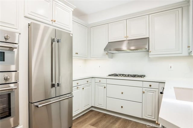 kitchen with appliances with stainless steel finishes, light countertops, under cabinet range hood, and white cabinetry