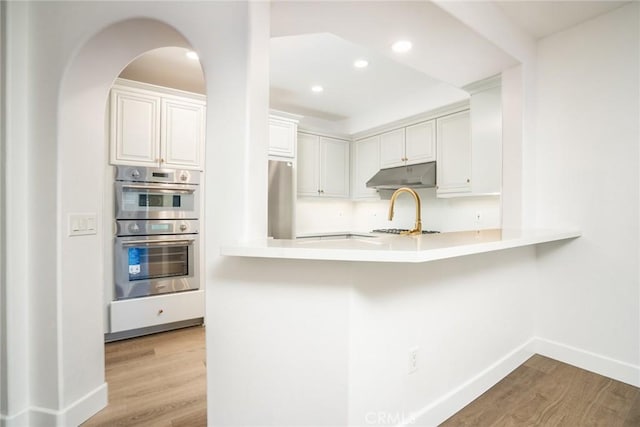 kitchen featuring light countertops, light wood-style flooring, appliances with stainless steel finishes, white cabinetry, and under cabinet range hood