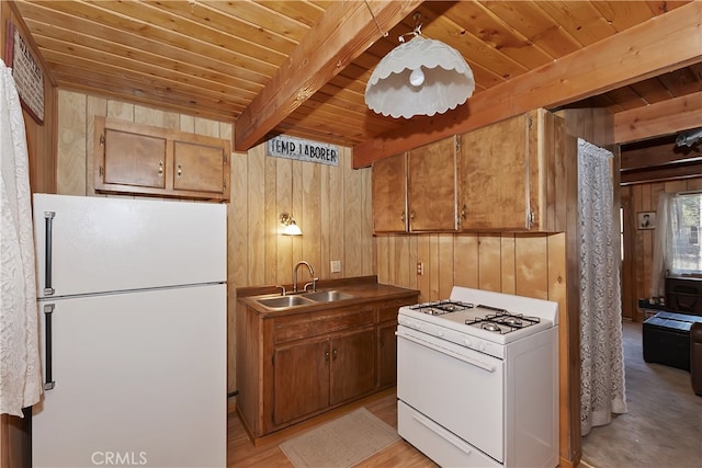 kitchen featuring hanging light fixtures, white appliances, a sink, and wooden walls