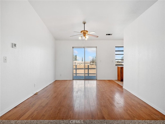 empty room featuring a ceiling fan, baseboards, visible vents, and wood finished floors