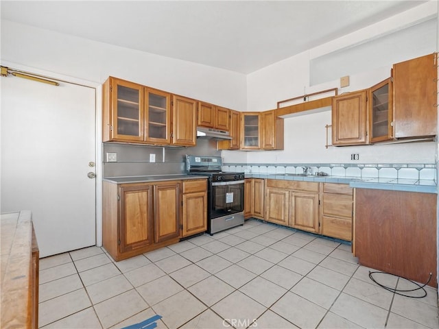 kitchen featuring glass insert cabinets, brown cabinetry, stainless steel range oven, and under cabinet range hood