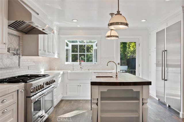 kitchen with a center island with sink, high end appliances, hanging light fixtures, a sink, and exhaust hood