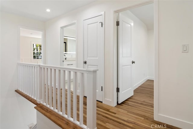 hallway with recessed lighting, wood finished floors, an upstairs landing, and baseboards