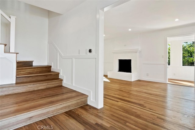 staircase with recessed lighting, a brick fireplace, wood finished floors, and a decorative wall