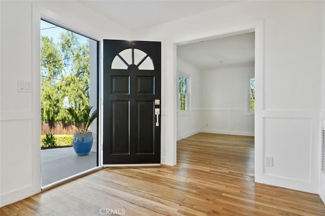 foyer entrance featuring light wood-style floors, a wainscoted wall, a decorative wall, and ornamental molding