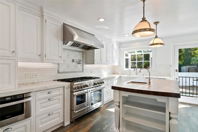 kitchen featuring wall chimney exhaust hood, butcher block countertops, appliances with stainless steel finishes, and white cabinets