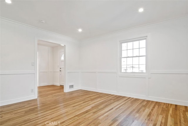 empty room featuring ornamental molding, light wood finished floors, and a decorative wall