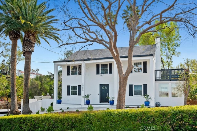 view of front facade featuring a chimney, fence, a balcony, and stucco siding