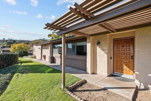 property entrance with stucco siding, a pergola, and a yard