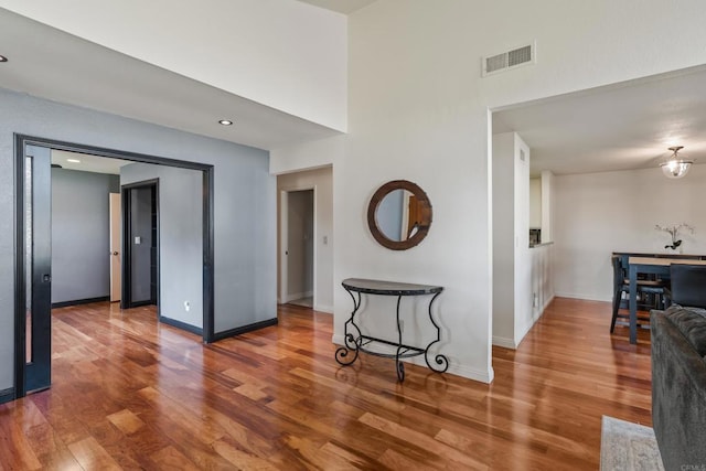 corridor with baseboards, a high ceiling, visible vents, and wood finished floors