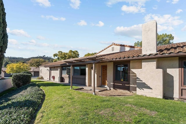 rear view of house featuring a yard, a tiled roof, stucco siding, a chimney, and a patio area