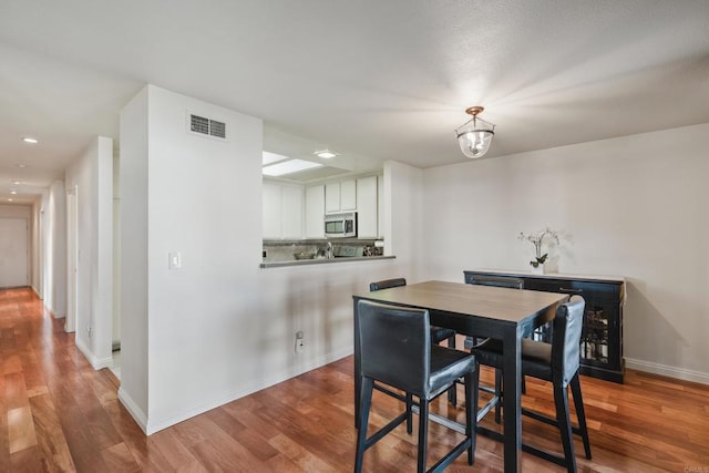 dining space with wood finished floors, visible vents, and baseboards