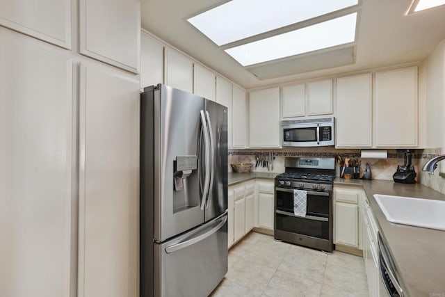 kitchen featuring stainless steel appliances, a sink, white cabinetry, light countertops, and tasteful backsplash