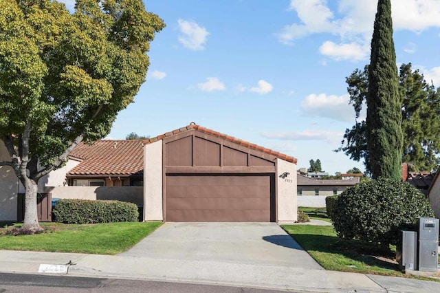 view of front of property featuring an attached garage, a front yard, concrete driveway, and a tiled roof