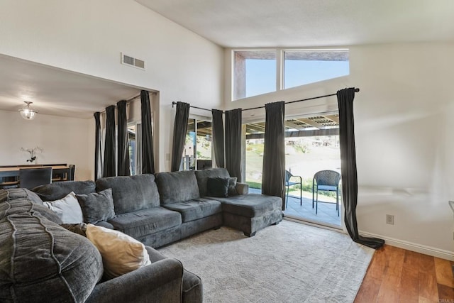 living area with high vaulted ceiling, visible vents, baseboards, and wood finished floors