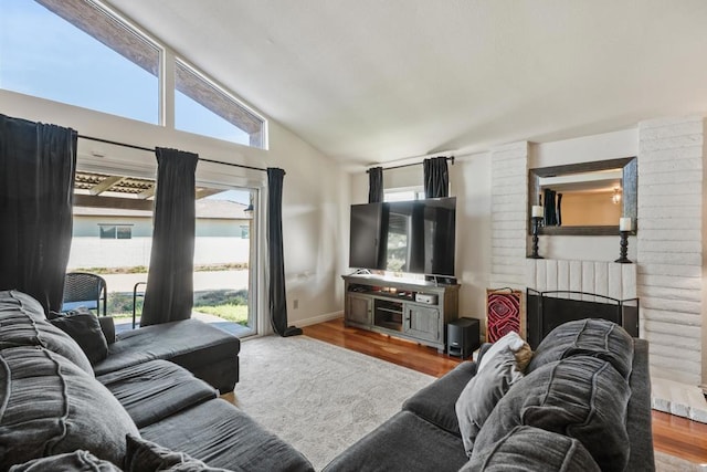 living area featuring vaulted ceiling, a brick fireplace, a wealth of natural light, and light wood-style floors