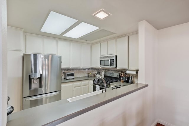 kitchen with tasteful backsplash, appliances with stainless steel finishes, light countertops, white cabinetry, and a sink