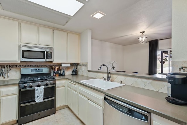 kitchen featuring light tile patterned floors, appliances with stainless steel finishes, a sink, light countertops, and backsplash