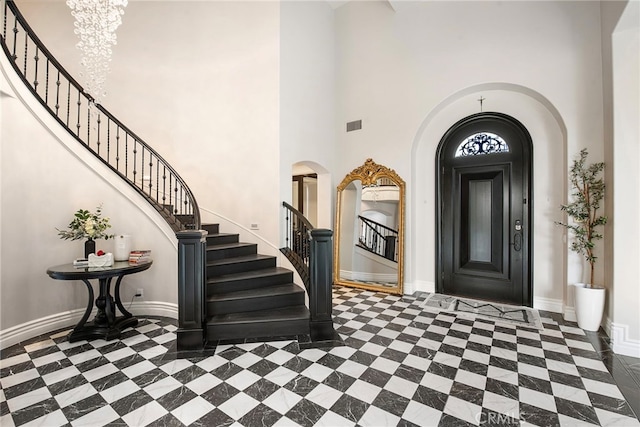 entrance foyer featuring arched walkways, visible vents, a towering ceiling, baseboards, and stairs