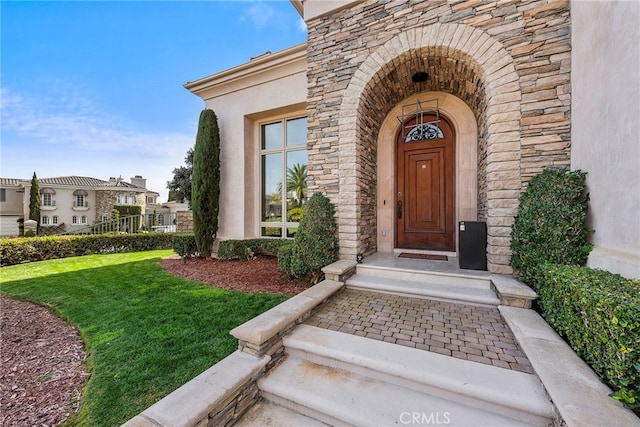 entrance to property featuring stone siding, a lawn, and stucco siding