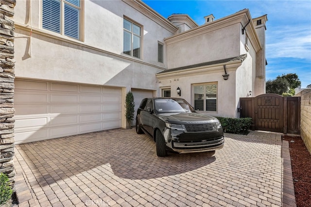 view of front of home with a garage, decorative driveway, a gate, and stucco siding