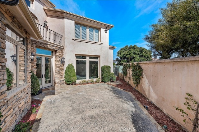 rear view of property with stucco siding, a patio area, fence, a balcony, and stone siding