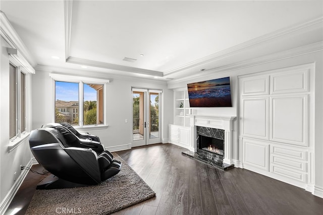 living room featuring a high end fireplace, a tray ceiling, french doors, and dark wood-style floors