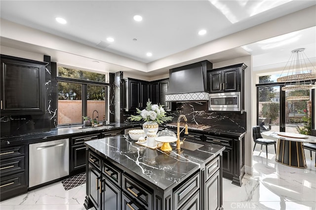 kitchen featuring stainless steel appliances, a sink, a kitchen island, wall chimney range hood, and dark cabinetry