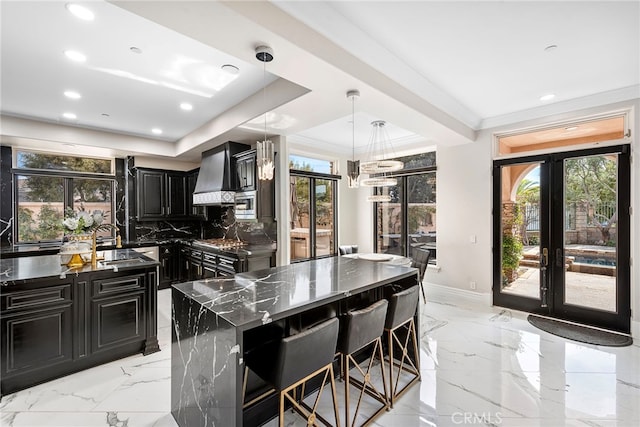 kitchen with dark cabinets, marble finish floor, french doors, custom exhaust hood, and a center island