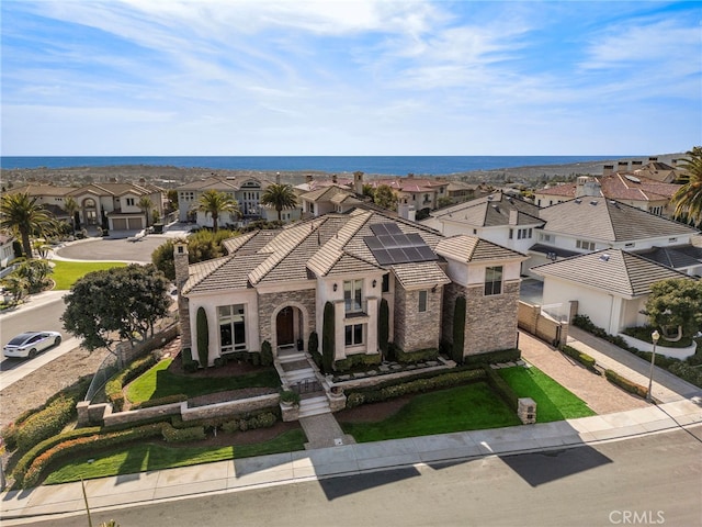 view of front facade featuring a tile roof, a chimney, a water view, a residential view, and stone siding