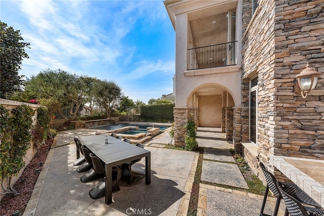 view of patio / terrace featuring a pool with connected hot tub, outdoor dining space, and a balcony