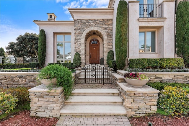 entrance to property with stone siding, a balcony, and stucco siding