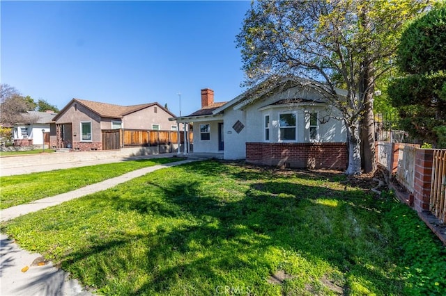 view of front of house with brick siding, a chimney, a front yard, and fence