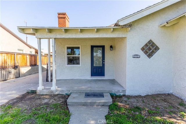 property entrance with covered porch, a chimney, fence, and stucco siding