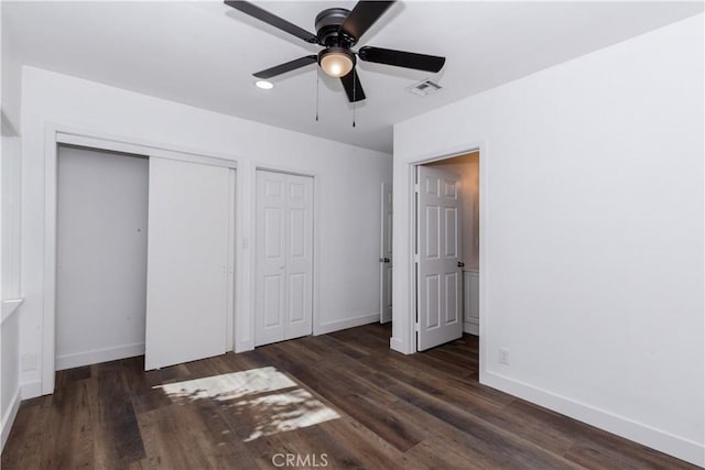 unfurnished bedroom with visible vents, dark wood finished floors, baseboards, and two closets