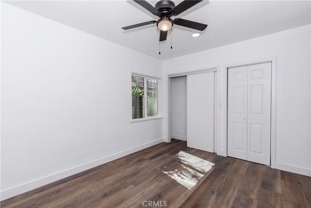 unfurnished bedroom with two closets, a ceiling fan, baseboards, and dark wood-style flooring