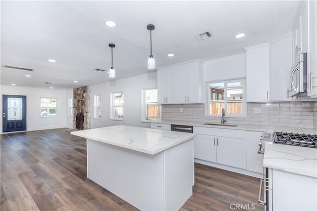 kitchen with appliances with stainless steel finishes, white cabinets, a sink, and a center island