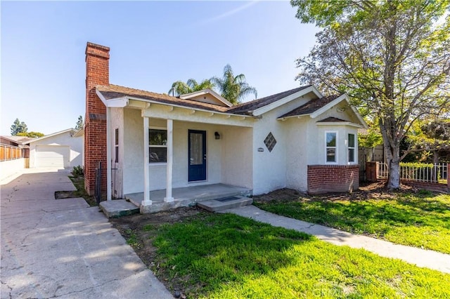 bungalow-style house with a porch, brick siding, stucco siding, a chimney, and a front yard