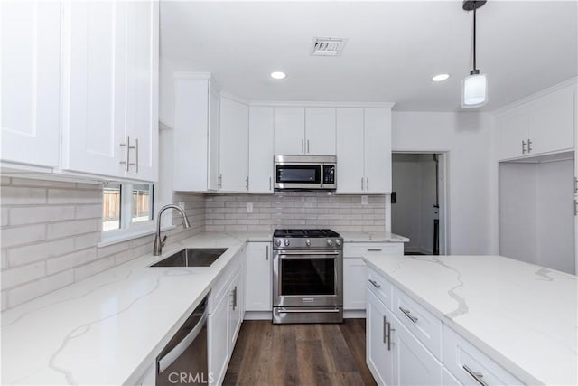 kitchen featuring hanging light fixtures, appliances with stainless steel finishes, white cabinets, a sink, and light stone countertops