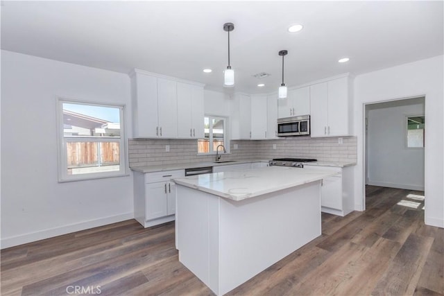 kitchen featuring a sink, white cabinets, backsplash, a center island, and stainless steel microwave