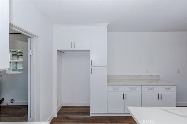 kitchen featuring light stone countertops, baseboards, dark wood-style floors, and white cabinets