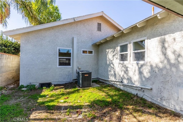 rear view of house featuring central AC unit, fence, and stucco siding