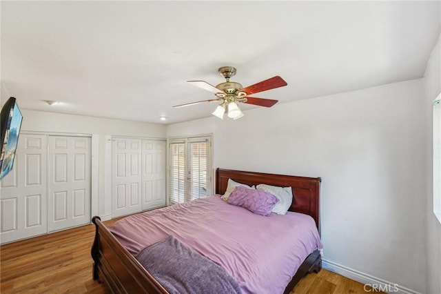 bedroom featuring two closets, a ceiling fan, baseboards, and wood finished floors