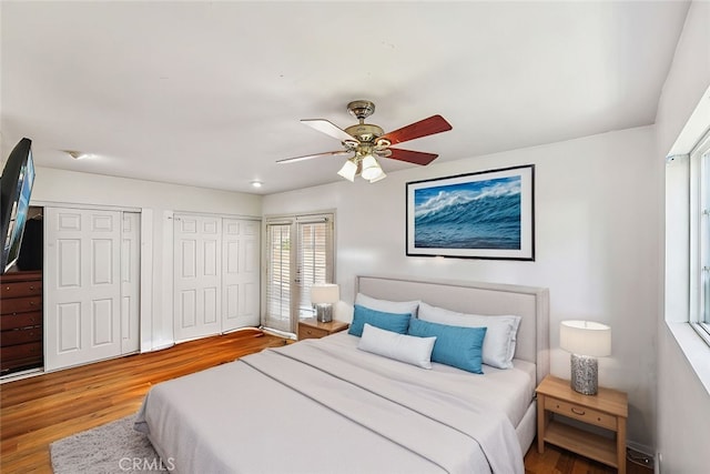 bedroom with ceiling fan, wood finished floors, and multiple closets